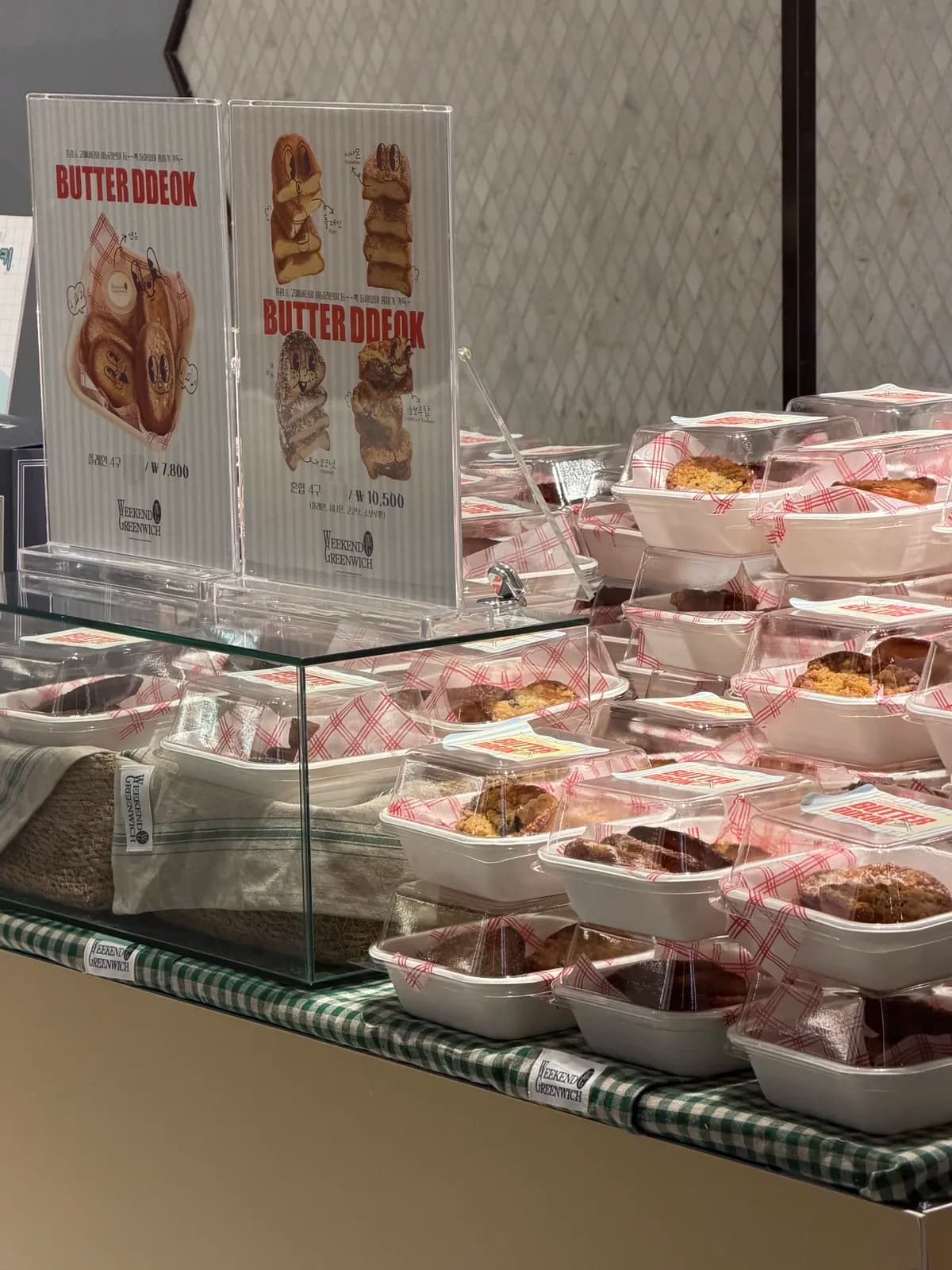 BUTTER DDEOK 가격 안내판 뒤로 포장된 버터떡이 쌓인 팝업 매대
